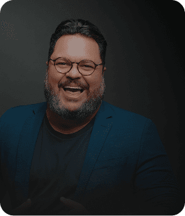 Evento Super Megavendas para concessionárias Um painel digital em cinza e preto com um homem sorridente de óculos, barbudo e camisa social azul. Ele aponta para o centro do painel, onde há vários cartões com textos como 'Equipe engajada', 'Clientes agendados' e 'Meta de vendas batida!'. Na parte inferior, há botões com os textos 'Ligar para cliente', 'Chamar no WhatsApp', 'Agendar tarefa', 'Registrar novo contato' e 'Ver convite'.